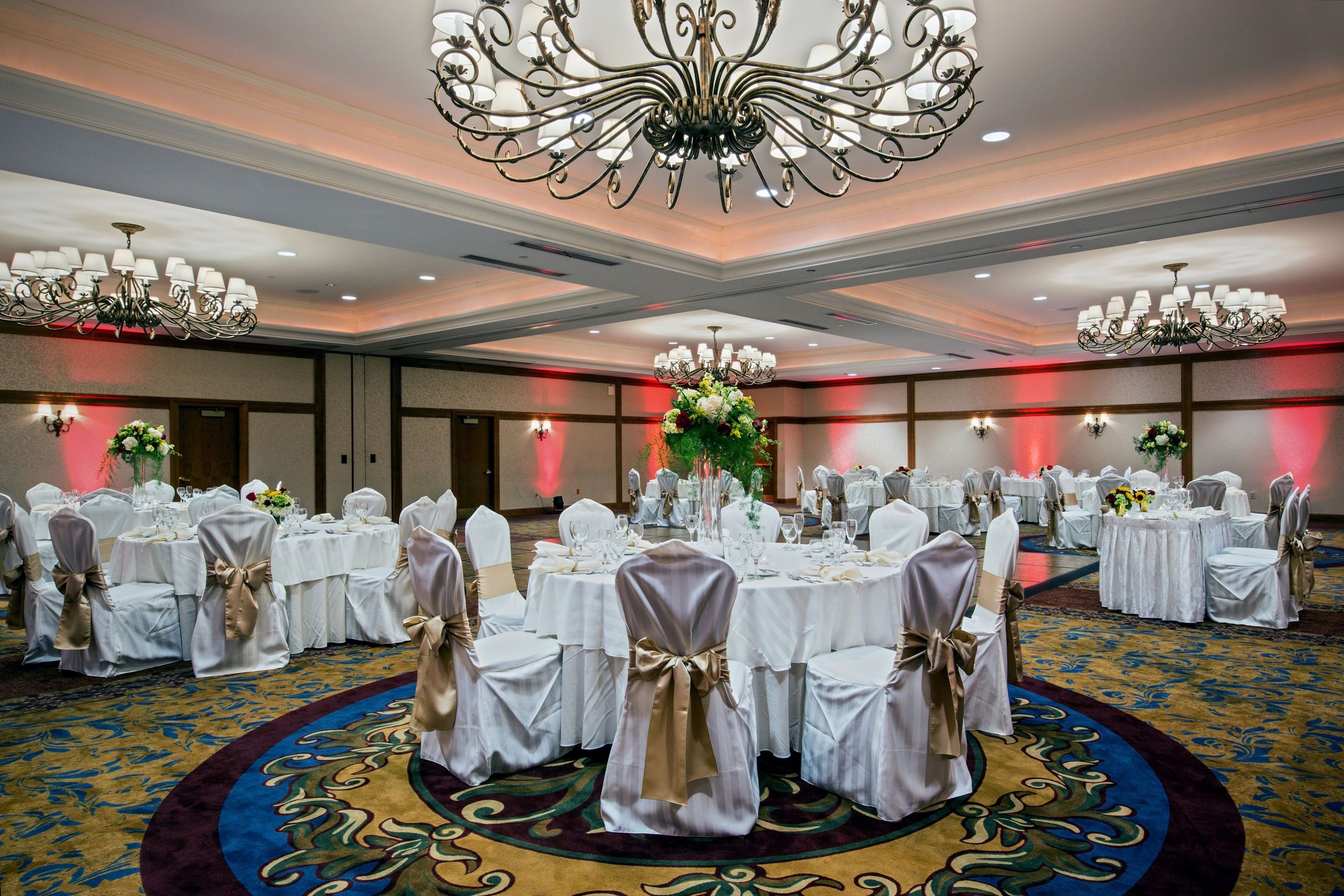 A banquet hall with round tables set for a formal event, featuring chandeliers and floral centerpieces.