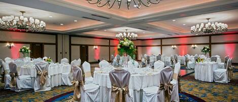 A banquet hall with round tables set for a formal event, featuring chandeliers and floral centerpieces.