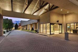 Entrada de hotel con un corredor cubierto, un mostrador de recepción y una puerta de cristal.