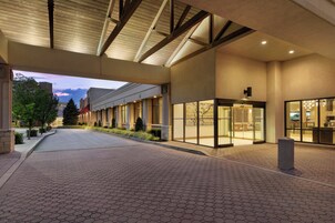 Entrada de hotel con un corredor cubierto, un mostrador de recepción y una puerta de cristal.