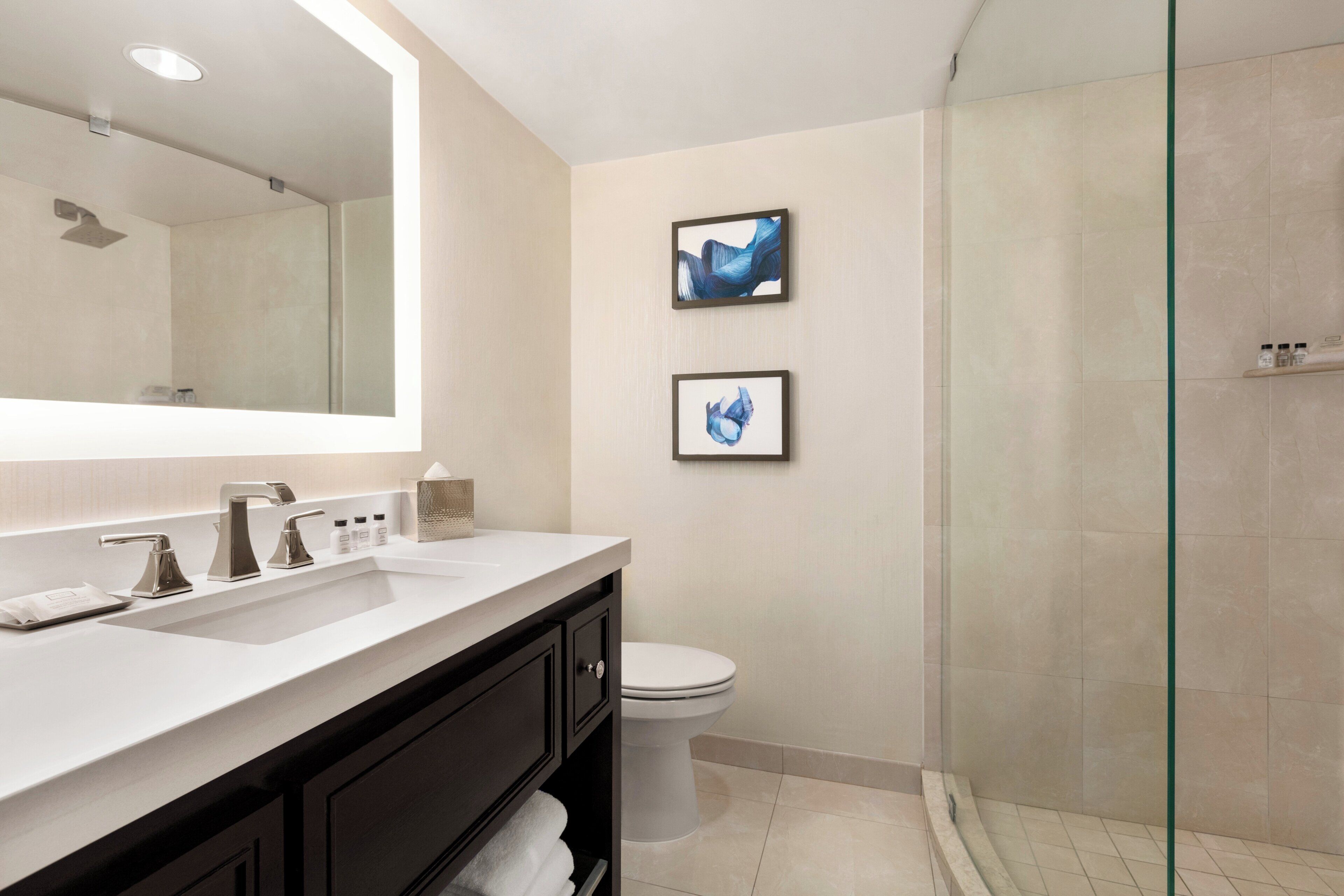 A modern bathroom with a large mirror, a white sink, a toilet, and a glass shower enclosure.