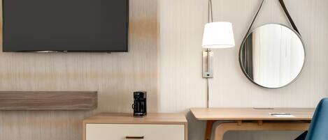 A hotel room with a flat-screen TV, a desk with a lamp, a chair, and a coffee maker.