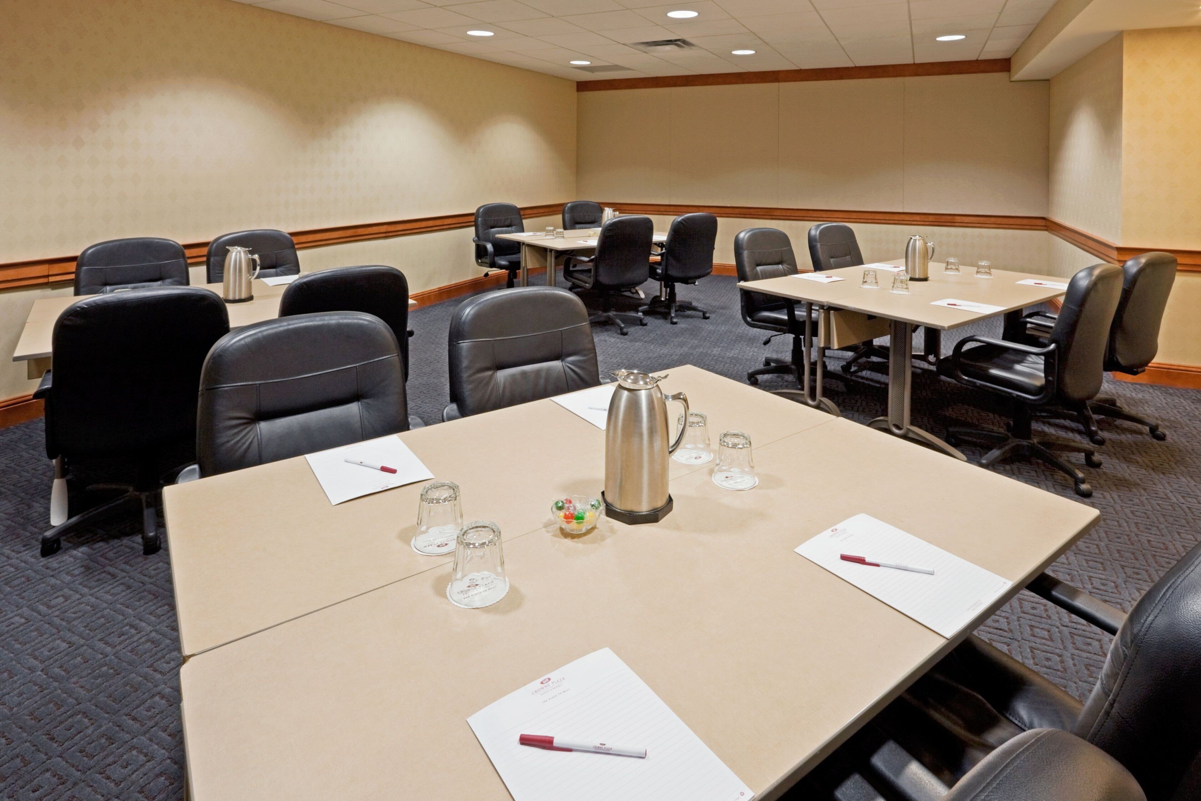 Un salón de conferencias con varias mesas, sillas y una cafetera en cada una.