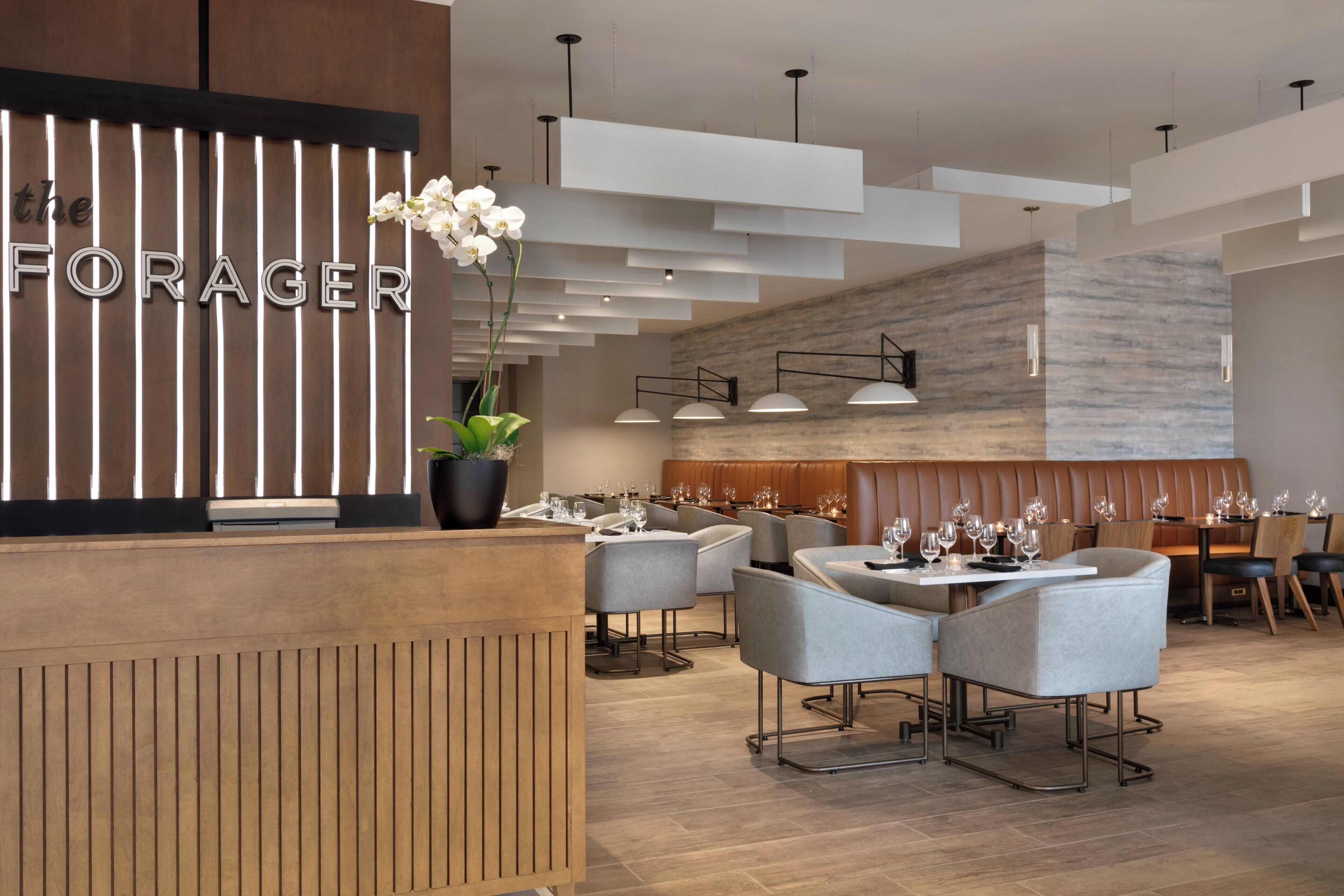 Un área de recepción de hotel moderna con un mostrador de madera, una planta en maceta y un espacio de estar con mesas y sillas.