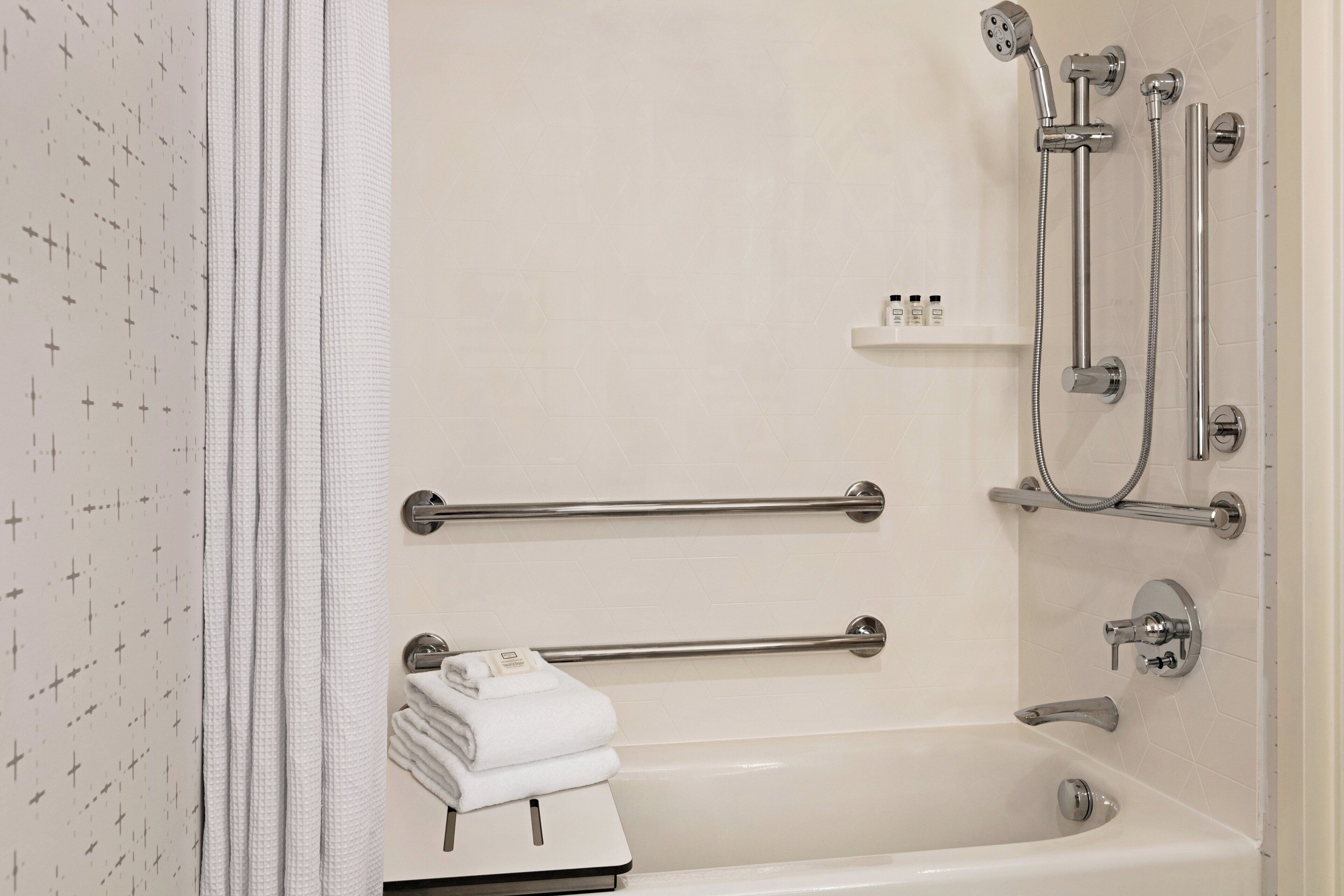 A bathroom with a bathtub, a shower, and handrails. There is a towel rack with folded towels.