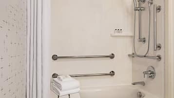 A bathroom with a bathtub, a shower, and handrails. There is a towel rack with folded towels.