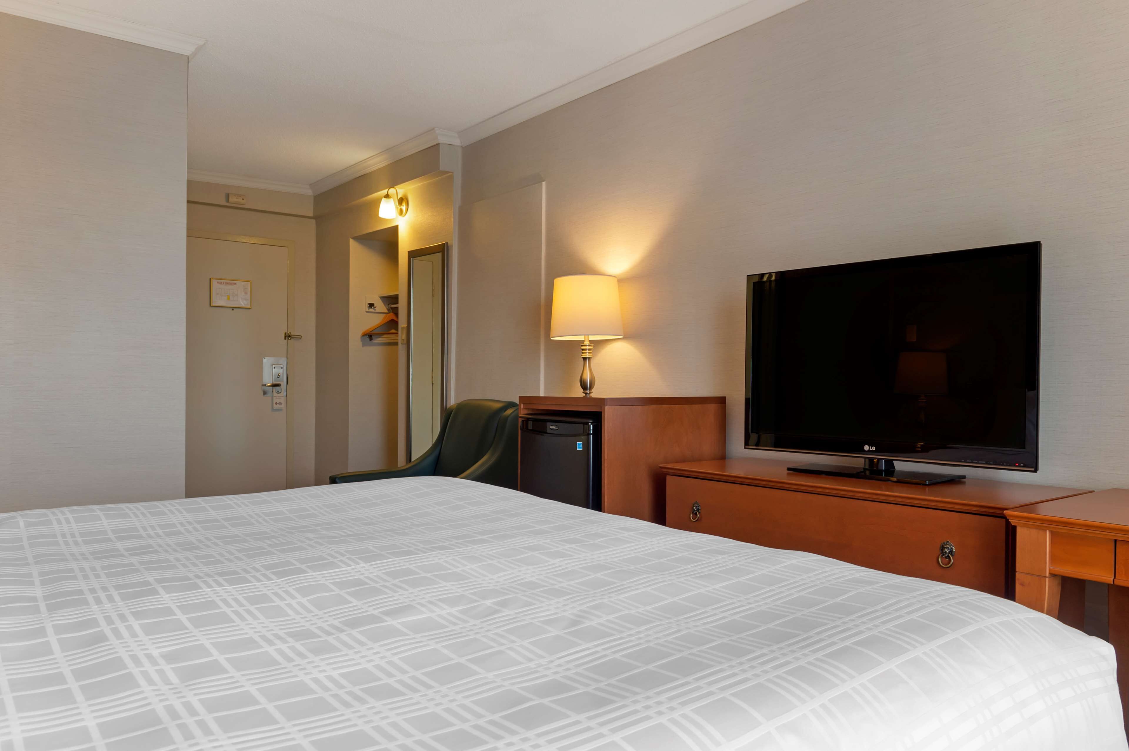 A hotel room with a large bed, a television on a wooden dresser, a desk, and a chair.