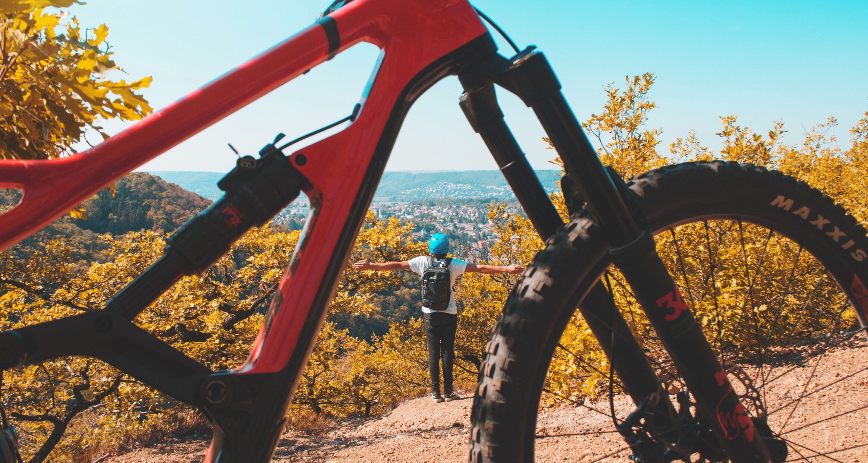 A mountain bike with a red frame and a person standing in the background with arms outstretched.