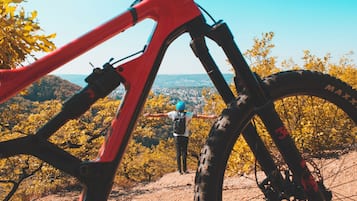 A mountain bike with a red frame and a person standing in the background with arms outstretched.