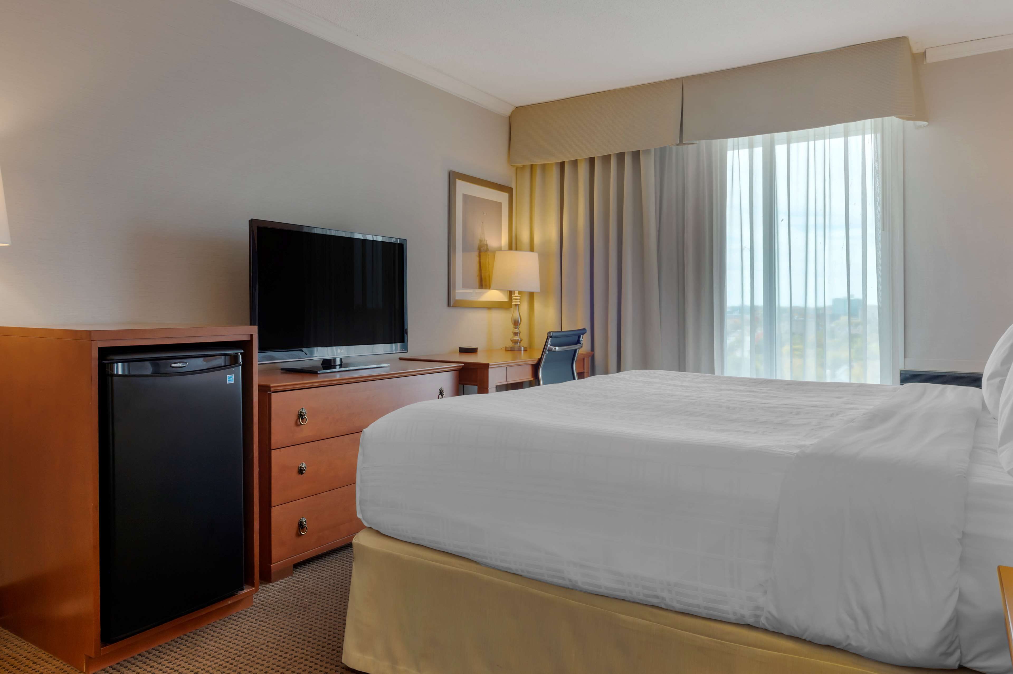 A hotel room with a bed, a television, a desk, and a minibar.