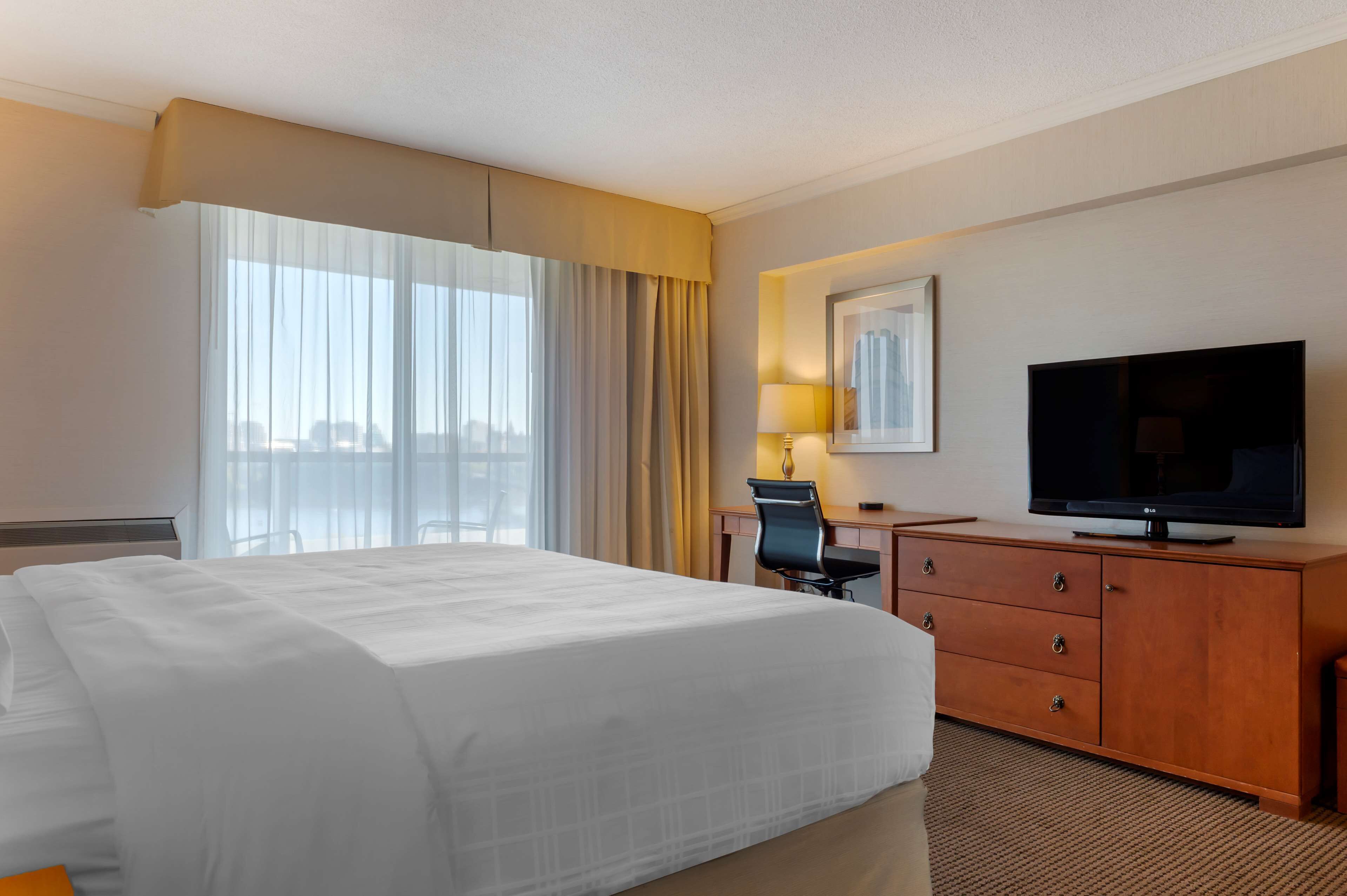 A hotel room with a large bed, a desk with a chair, a television, and a window with curtains.