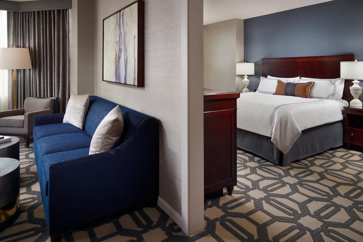 Une chambre d’hôtel avec un canapé bleu, un lit avec une literie blanche, une tête de lit en bois et une moquette à motifs.