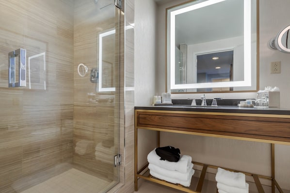 A modern bathroom with a glass shower enclosure, a vanity with a large mirror, and neatly folded towels on a shelf. - Omni Richmond Hotel (Richmond)