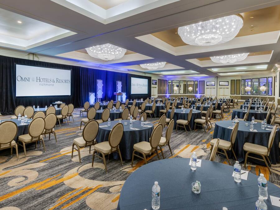 A conference room with multiple tables and chairs, a large screen, and a chandelier.
