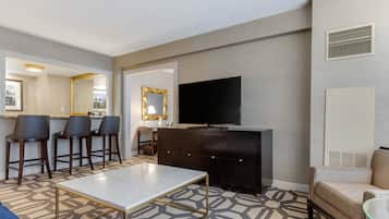 A modern hotel room with a dining area, a flat-screen TV, a sofa, and a patterned carpet.