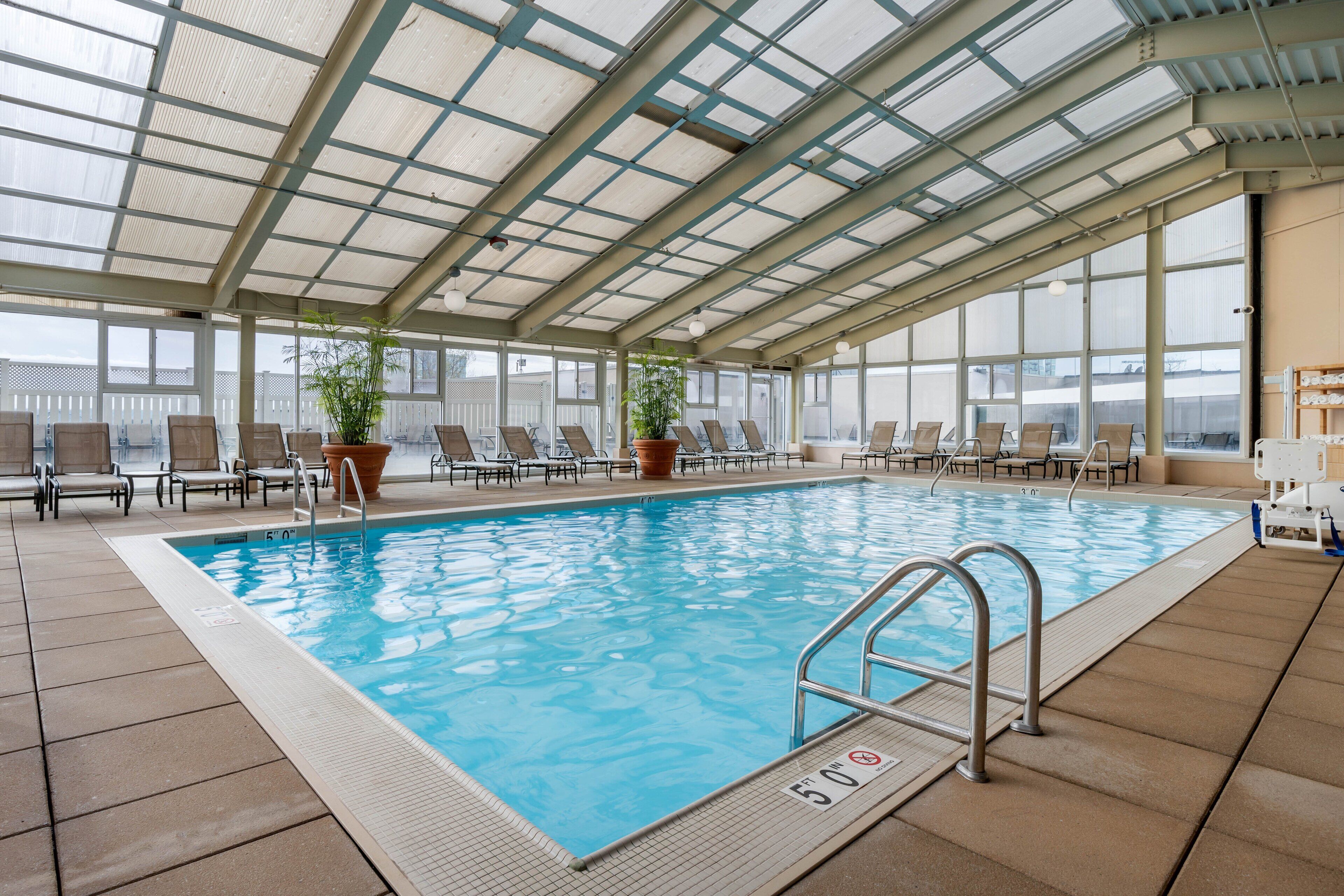Una piscina interior con agua azul cristalina, rodeada de sillones de descanso y plantas en macetas.