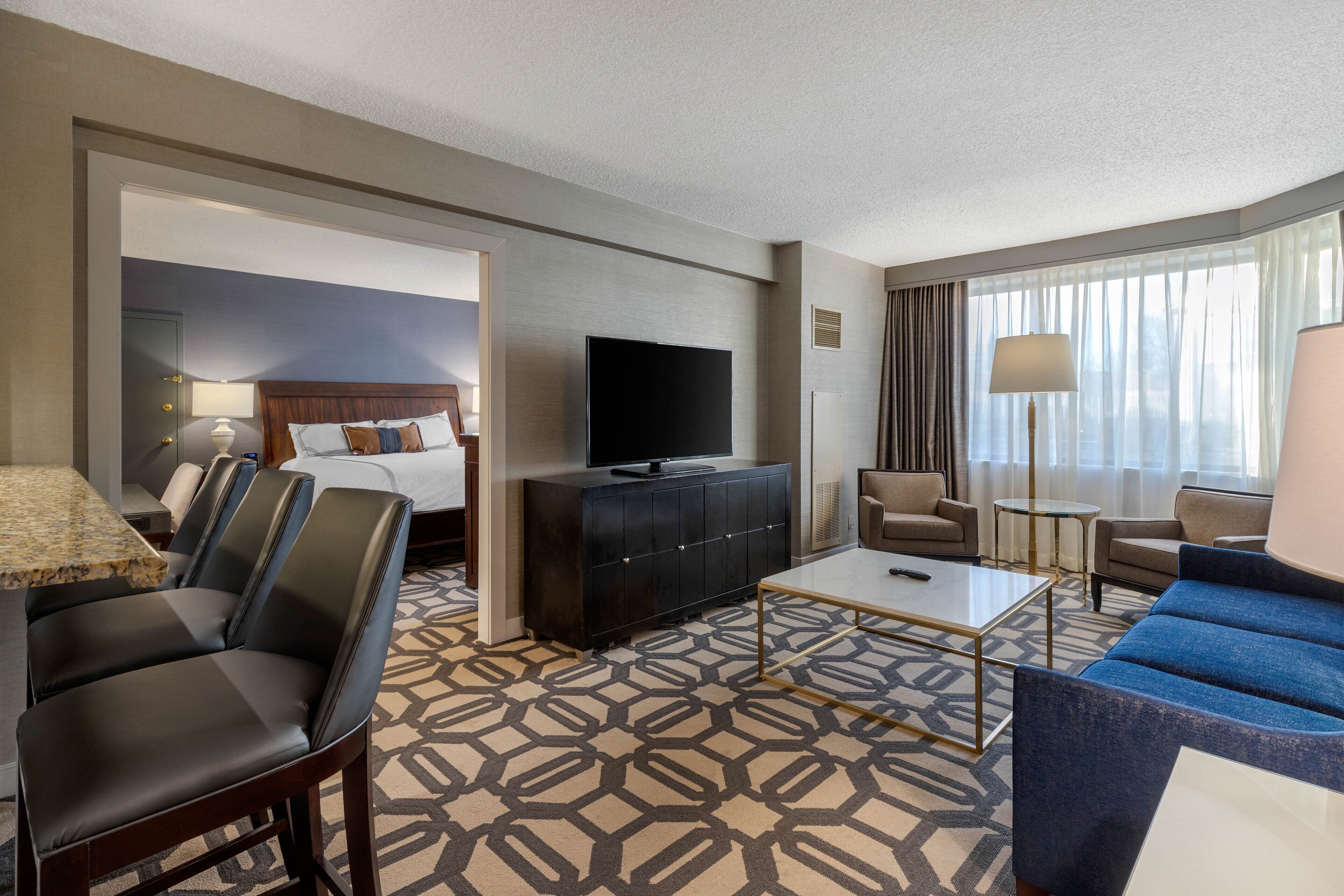 A hotel room with a bed, a TV, a coffee table, and seating area.