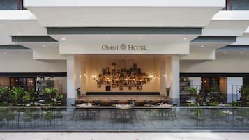 Exterior del hotel Omni, de diseño moderno, con un amplio espacio de estar con mesas y sillas, y diversos maceteros alrededor del perímetro.