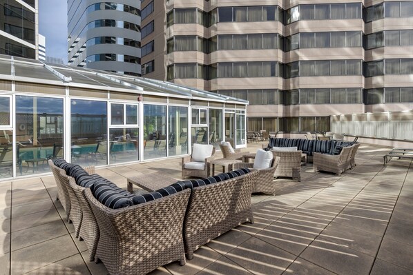 A rooftop patio with wicker furniture and glass doors overlooking a pool and cityscape. - Omni Richmond Hotel (Richmond)