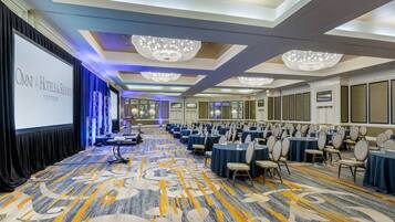 Une salle de conférence dotée d’un grand écran affichant le texte « OMNI HOTELS & RESORTS Richmond », de rangées de tables avec des chaises et de lustres au plafond.