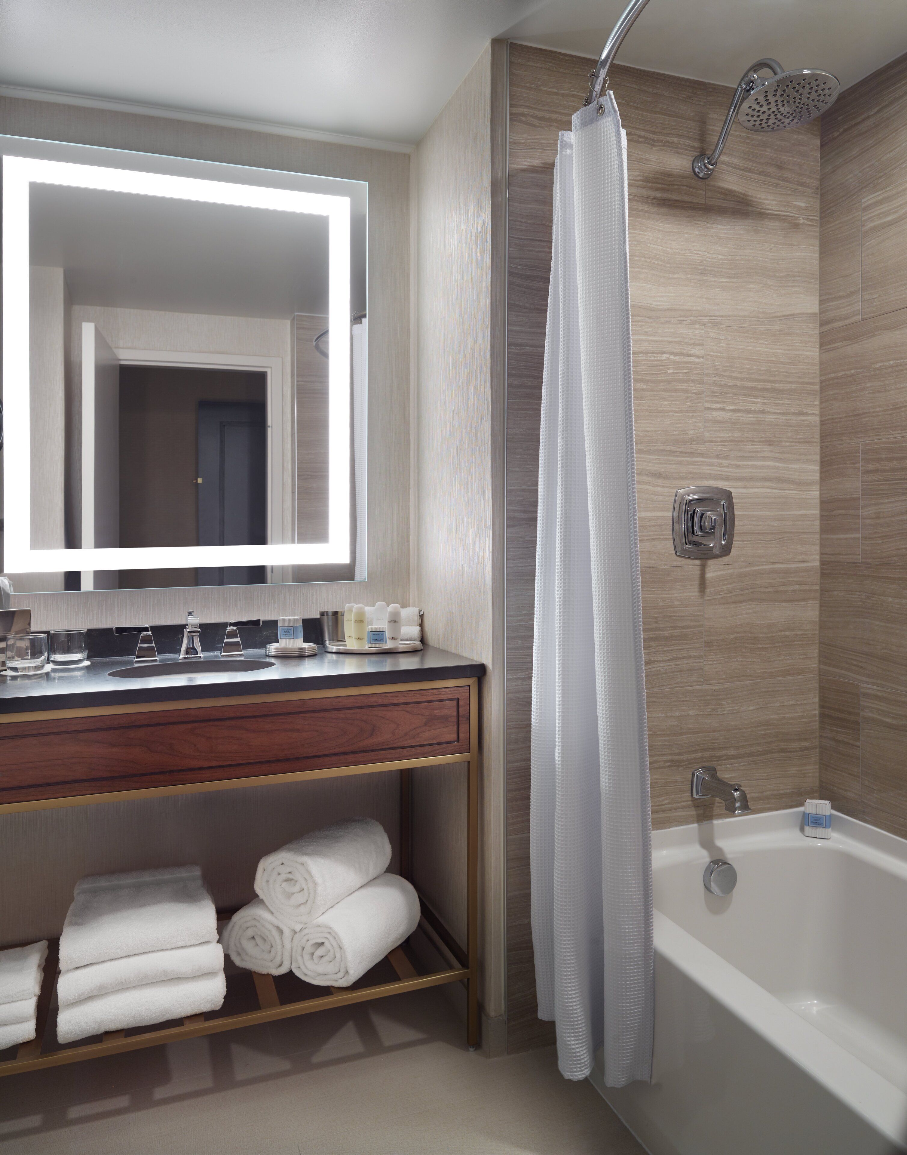 A modern bathroom with a vanity, mirror, shower, and towels.