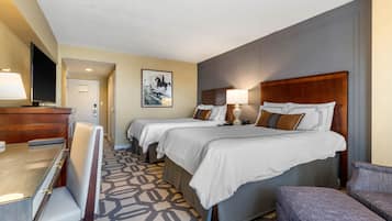 A hotel room with two beds, a desk, a chair, and a television.