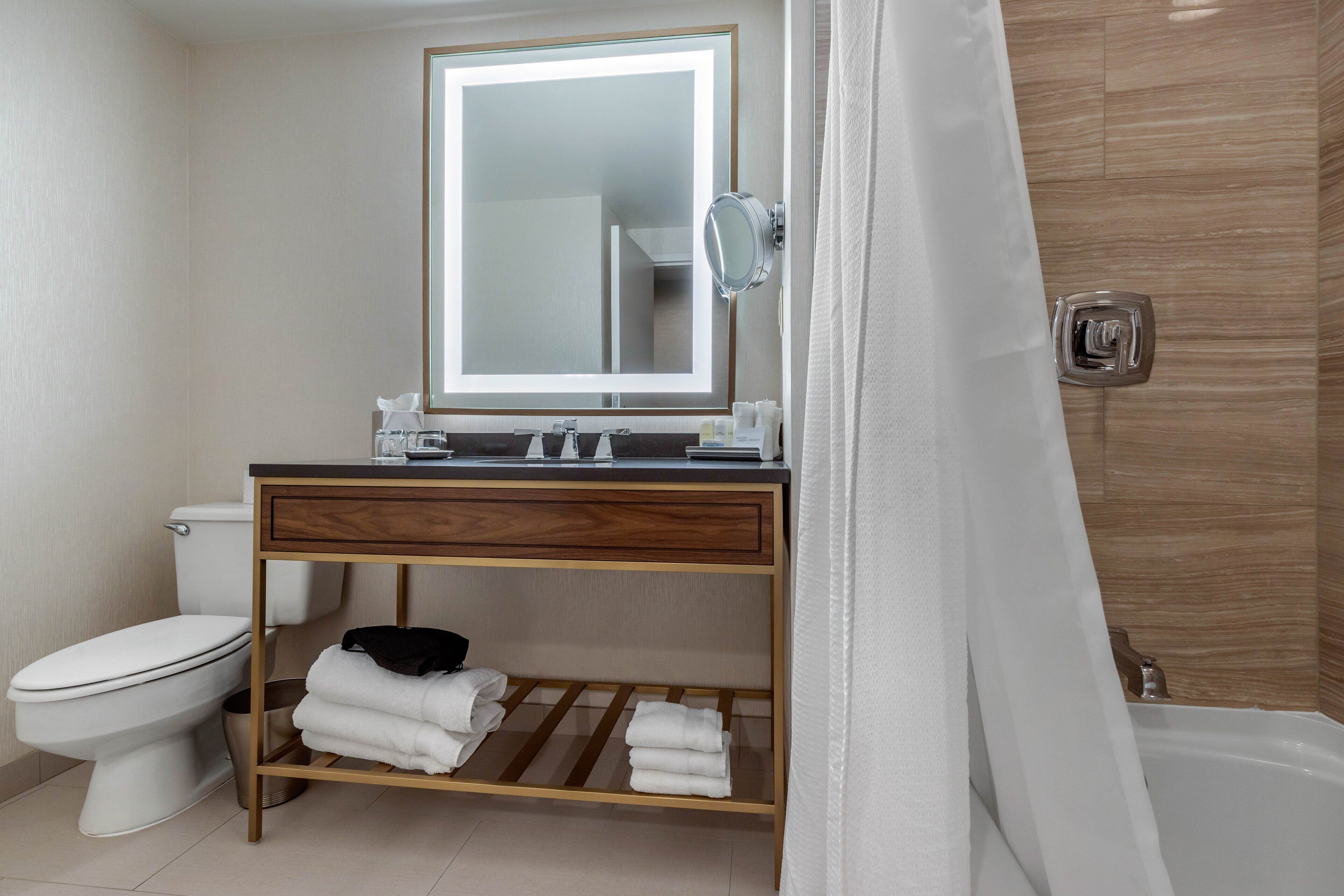 A modern bathroom with a wooden vanity, a large mirror, a toilet, and a shower area.