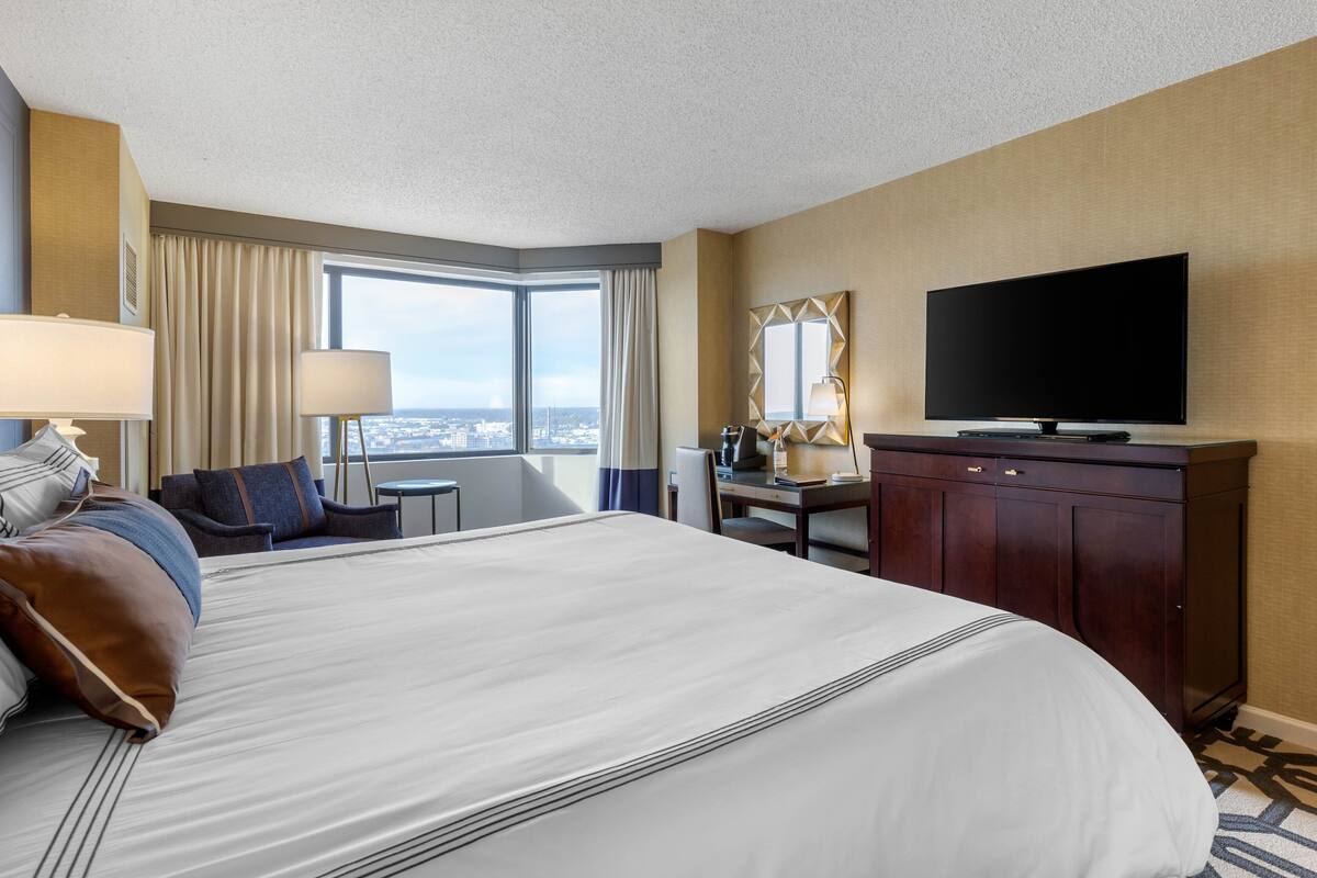Een hotelkamer met een groot bed, een bureau, een televisie en uitzicht op de stad.