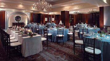 A banquet hall with multiple round tables, each set with chairs and tablecloths, and a large chandelier hanging from the ceiling.
