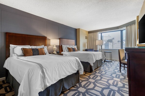 A hotel room with two beds, a desk, a chair, and a large window with a city view. - Omni Richmond Hotel (Richmond)