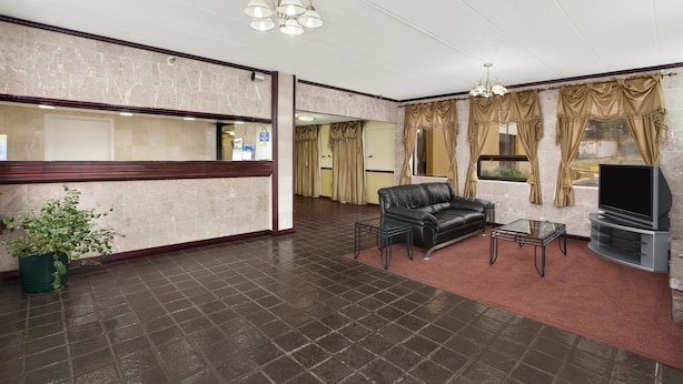 A hotel lobby with a reception desk, a leather sofa, a glass coffee table, and a TV on a stand. - Days Inn by Wyndham Hagerstown I-70 (Hagerstown)