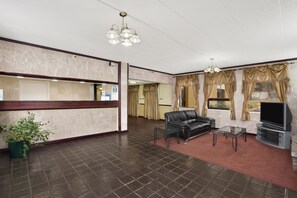 A hotel lobby with a reception desk, a leather sofa, a glass coffee table, and a TV on a stand. - Days Inn by Wyndham Hagerstown I-70 (Hagerstown)