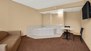 A hotel room with a brown carpet, a white bathtub, a white round table, and two chairs. - Days Inn by Wyndham Hagerstown I-70 (Hagerstown)