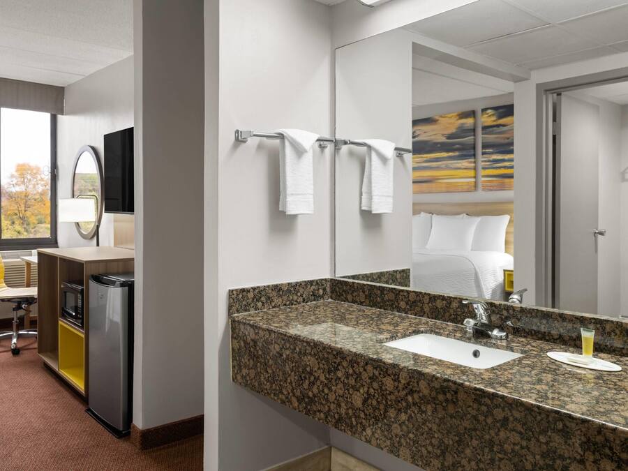 A hotel bathroom with a granite countertop sink, a mirror, and a towel rack.