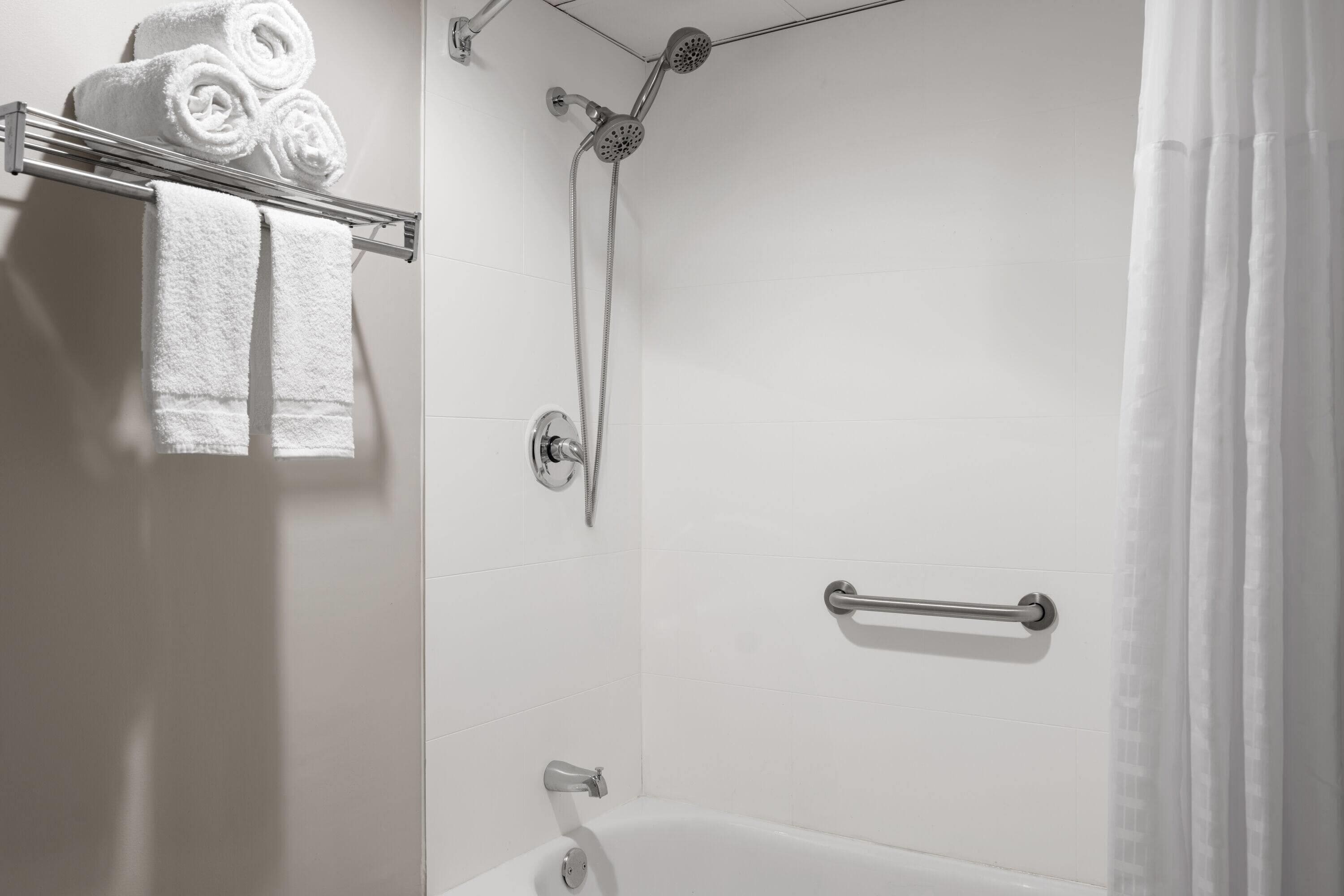 Een moderne badkamer met een douche, een bad en een handdoekrek met opgerolde handdoeken.