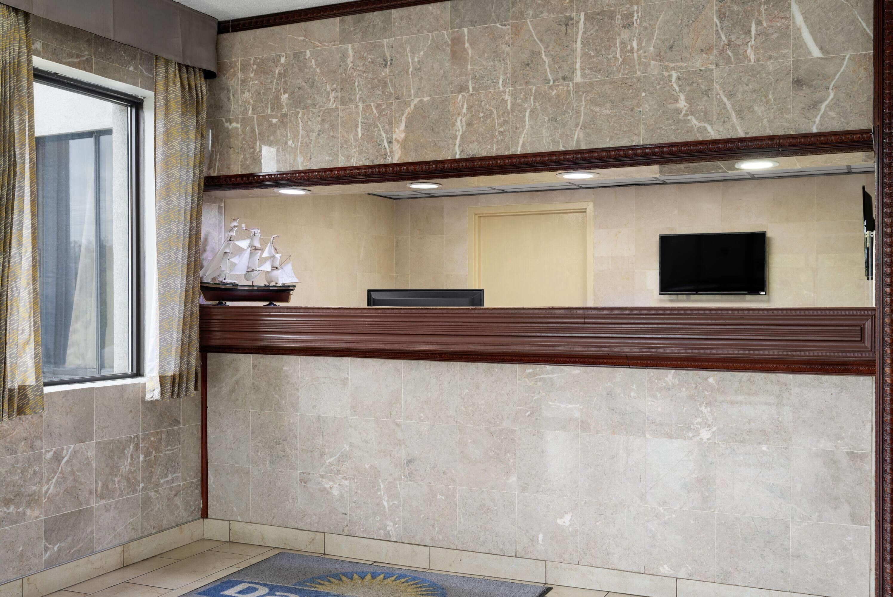 Una zona de recepción con pared de mármol, mostrador de madera, modelo de barco, televisor y una puerta.