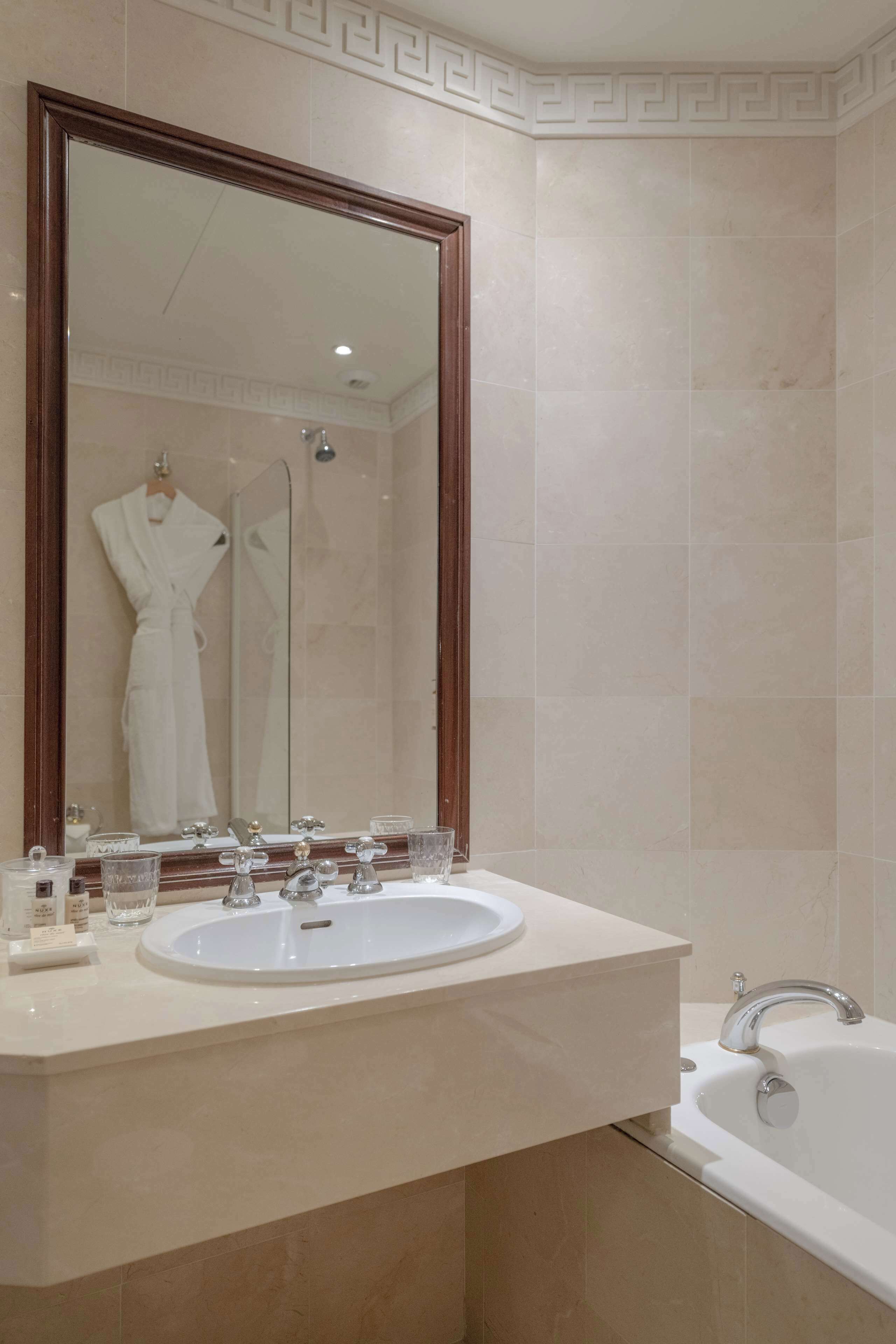 A bathroom with a large mirror, a sink, and a bathtub.
