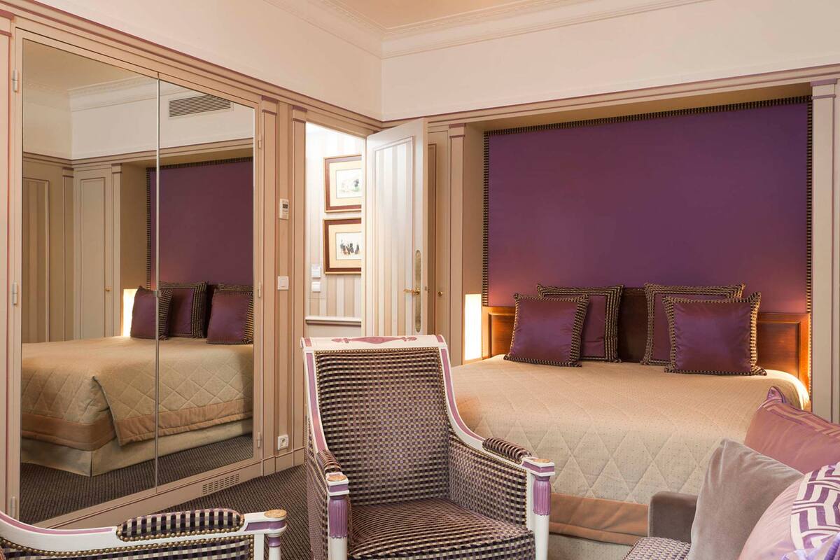 Une chambre d’hôtel avec un lit, une chaise, un miroir et une armoire.