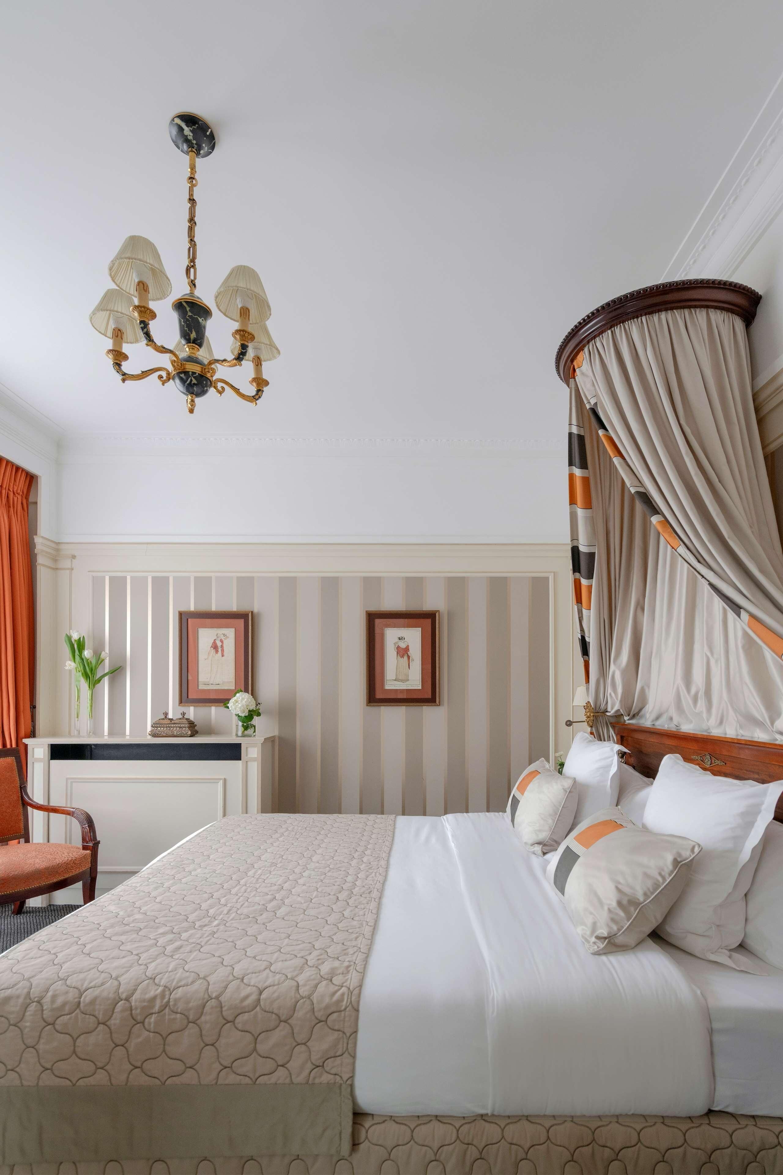 Une chambre à coucher avec un lit à baldaquin, un lustre, une coiffeuse avec un miroir et un papier peint à rayures.