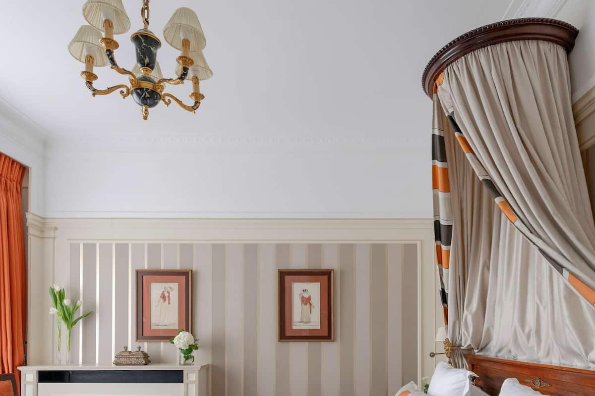 Une chambre à coucher avec un lit à baldaquin, un lustre, une coiffeuse avec un miroir et un papier peint à rayures.