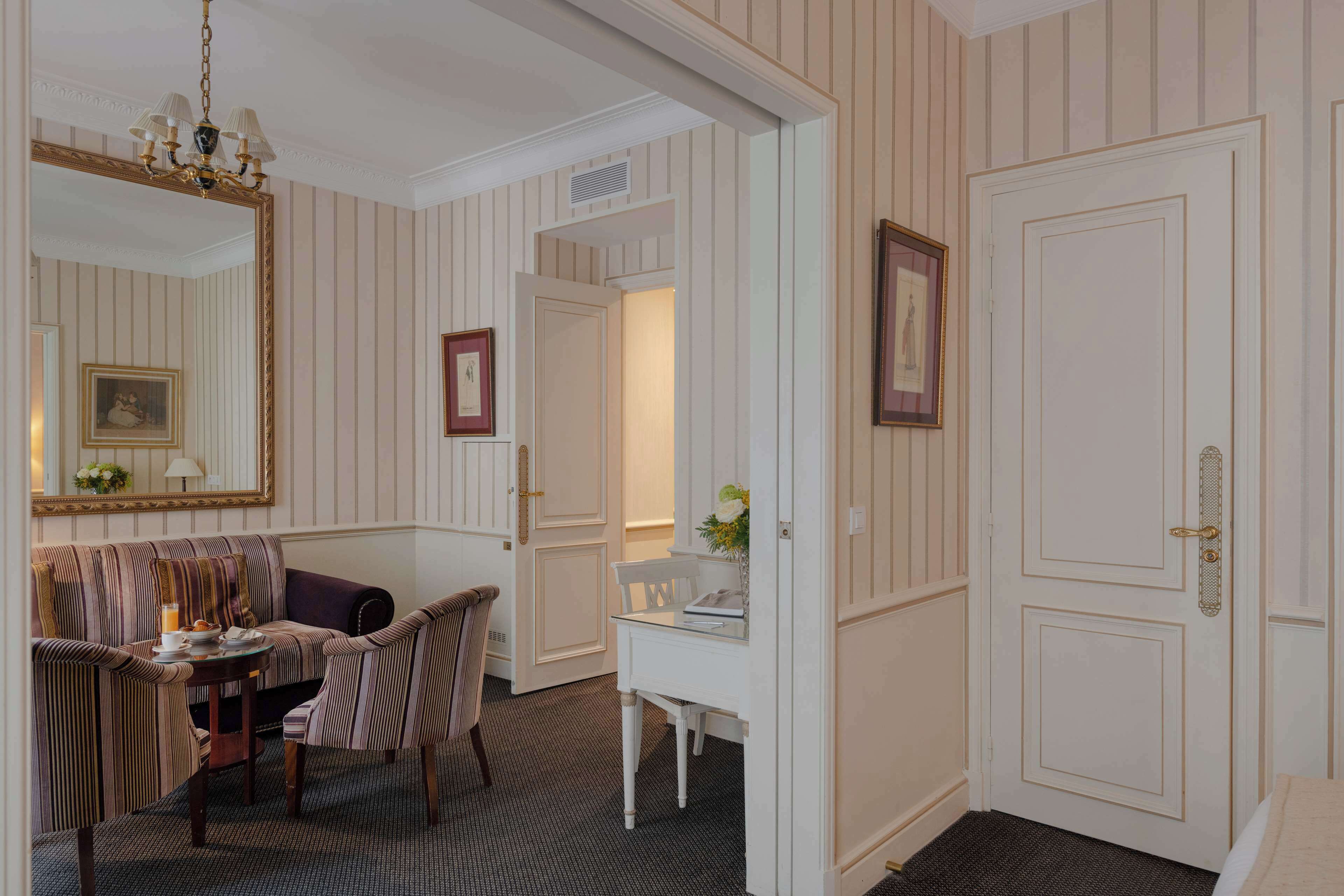 A room with a striped wall, a sofa, a dining table with chairs, a small white desk, and a door.