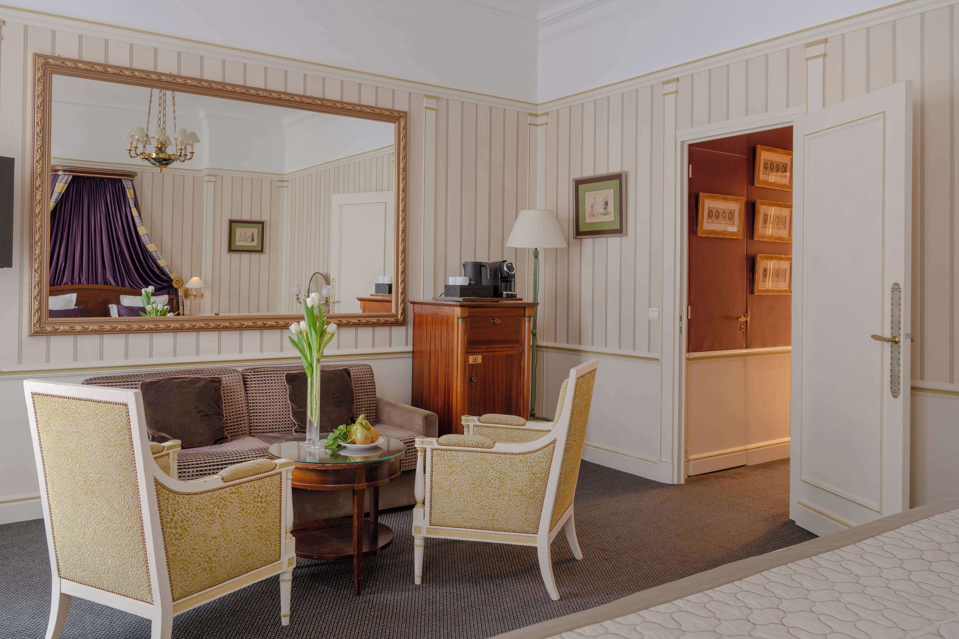 Hotelkamer met een grote spiegel, een bank, twee fauteuils, een salontafel en een kast.