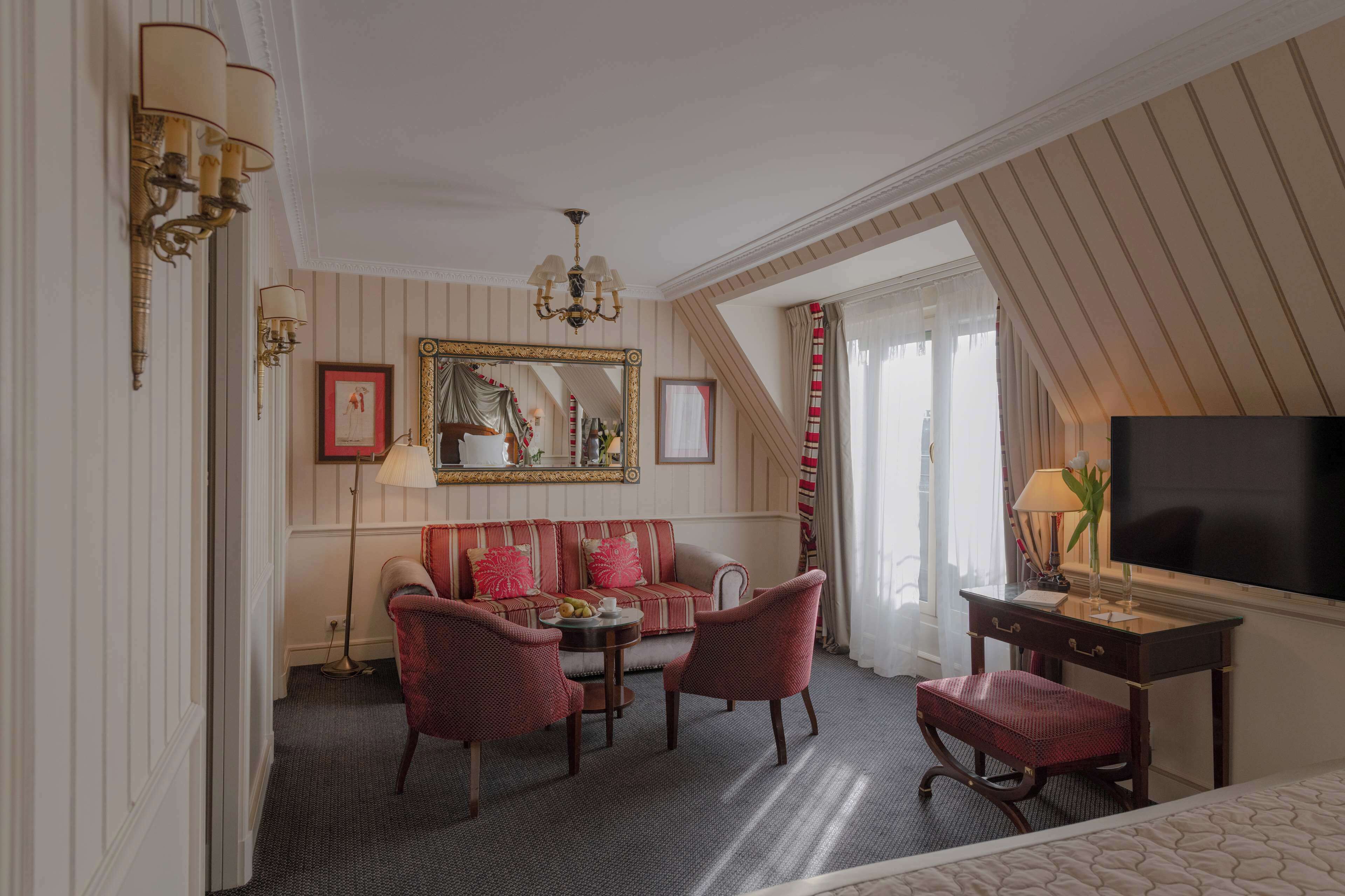 A hotel room with a sofa, chairs, a desk, a TV, and a large mirror.