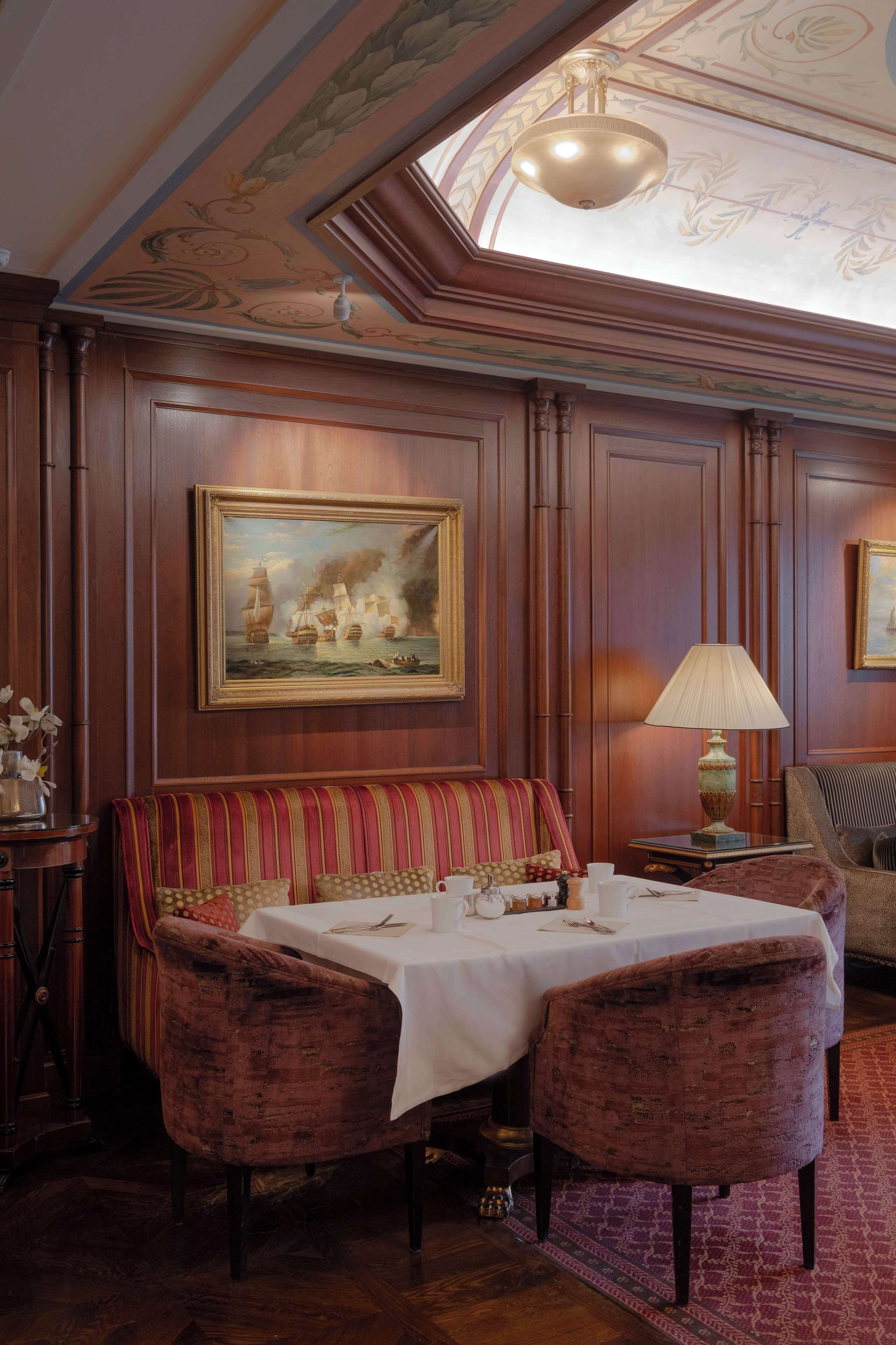 A dining area with a wooden table, two upholstered chairs, a striped sofa, and a painting of a ship on the wall.