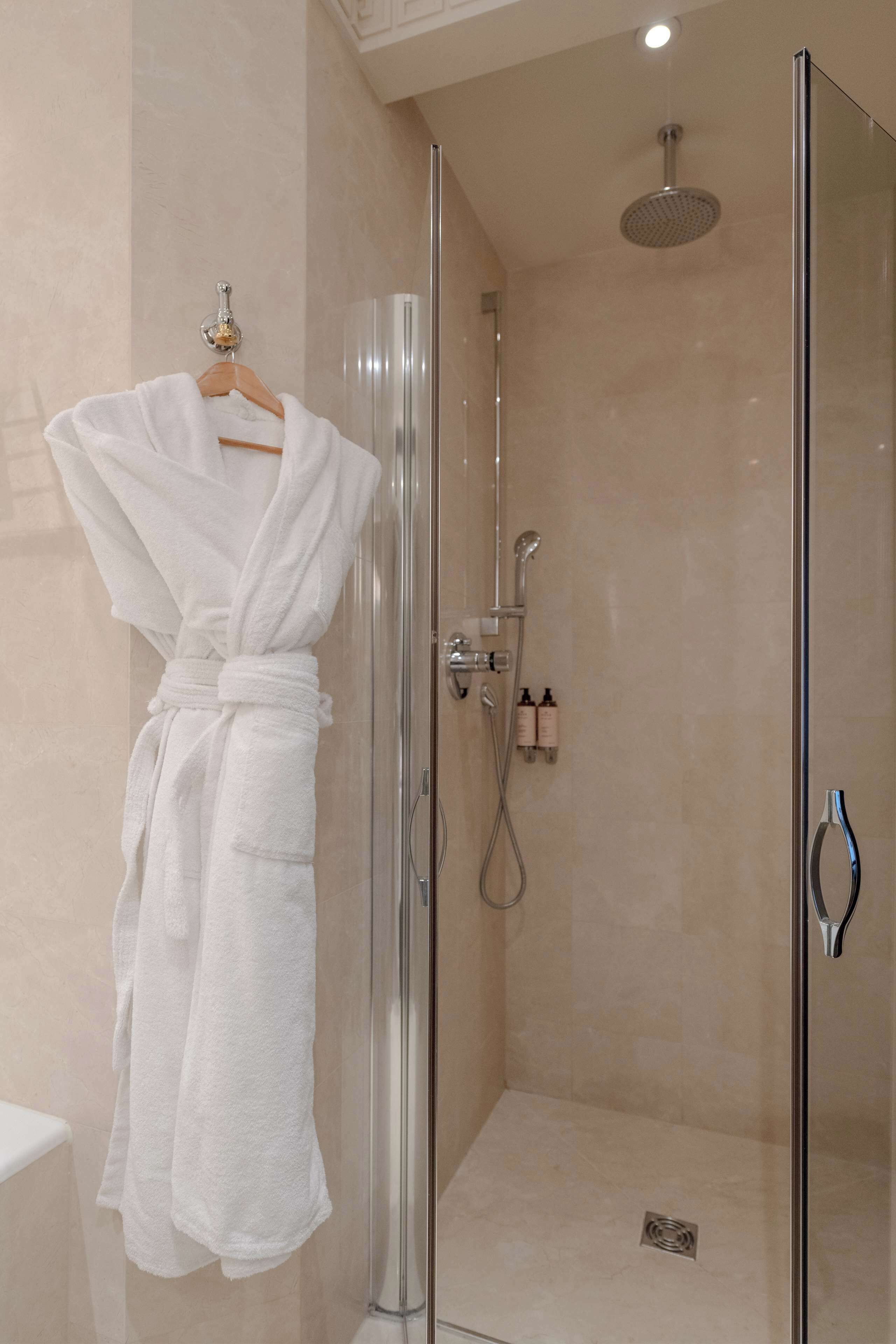 Une douche fermée par des parois en verre, dotée d’un pommeau de douche à main et d’un robinet mural.