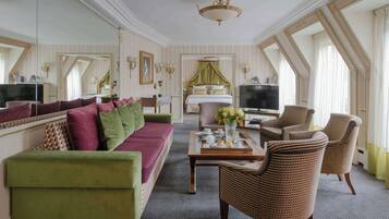 Habitación de hotel con sofá verde, sillas de mimbre, cama con dosel, televisor y un espejo grande.