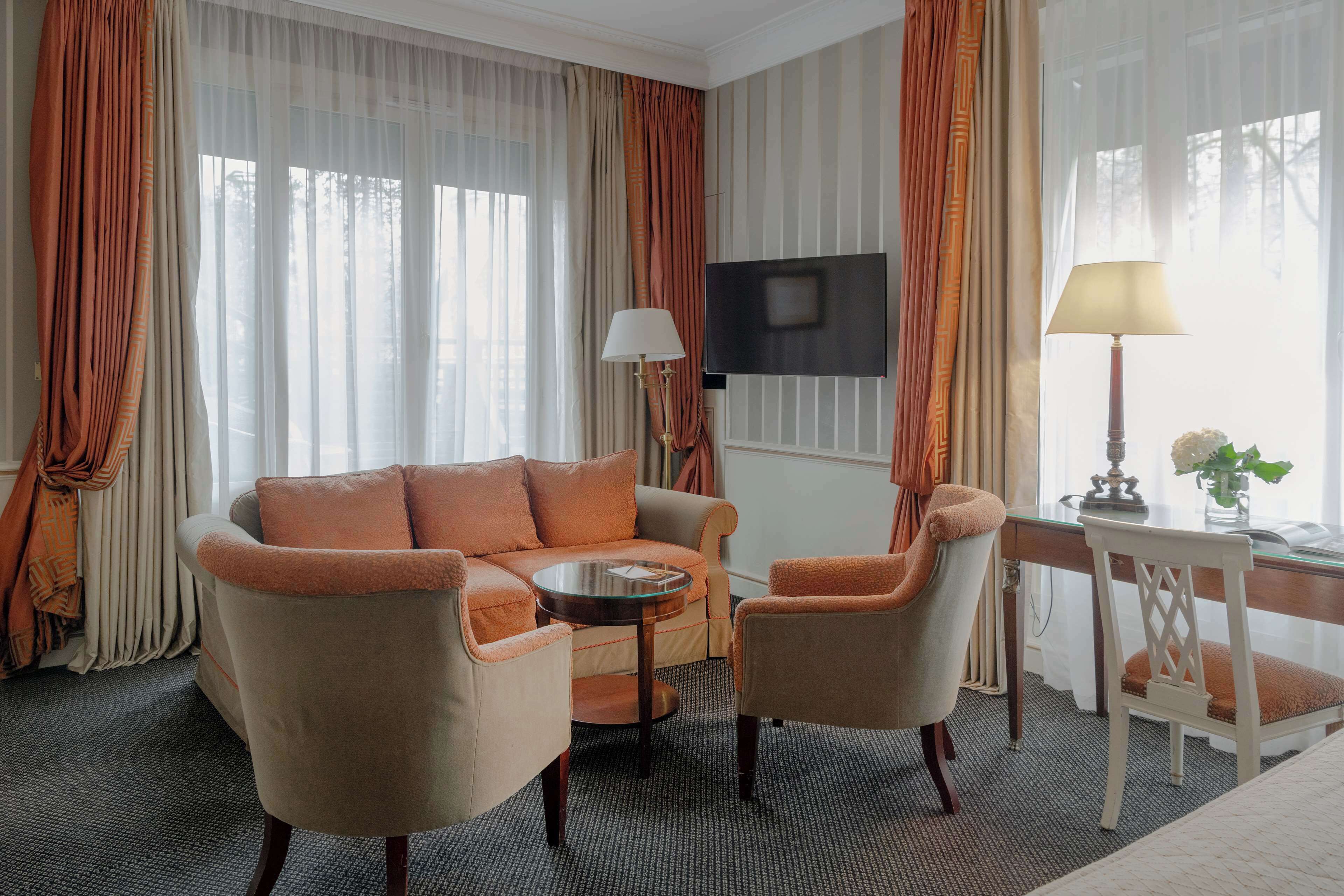 Une chambre d’hôtel avec un canapé, deux fauteuils, une petite table, une télévision et une lampe.