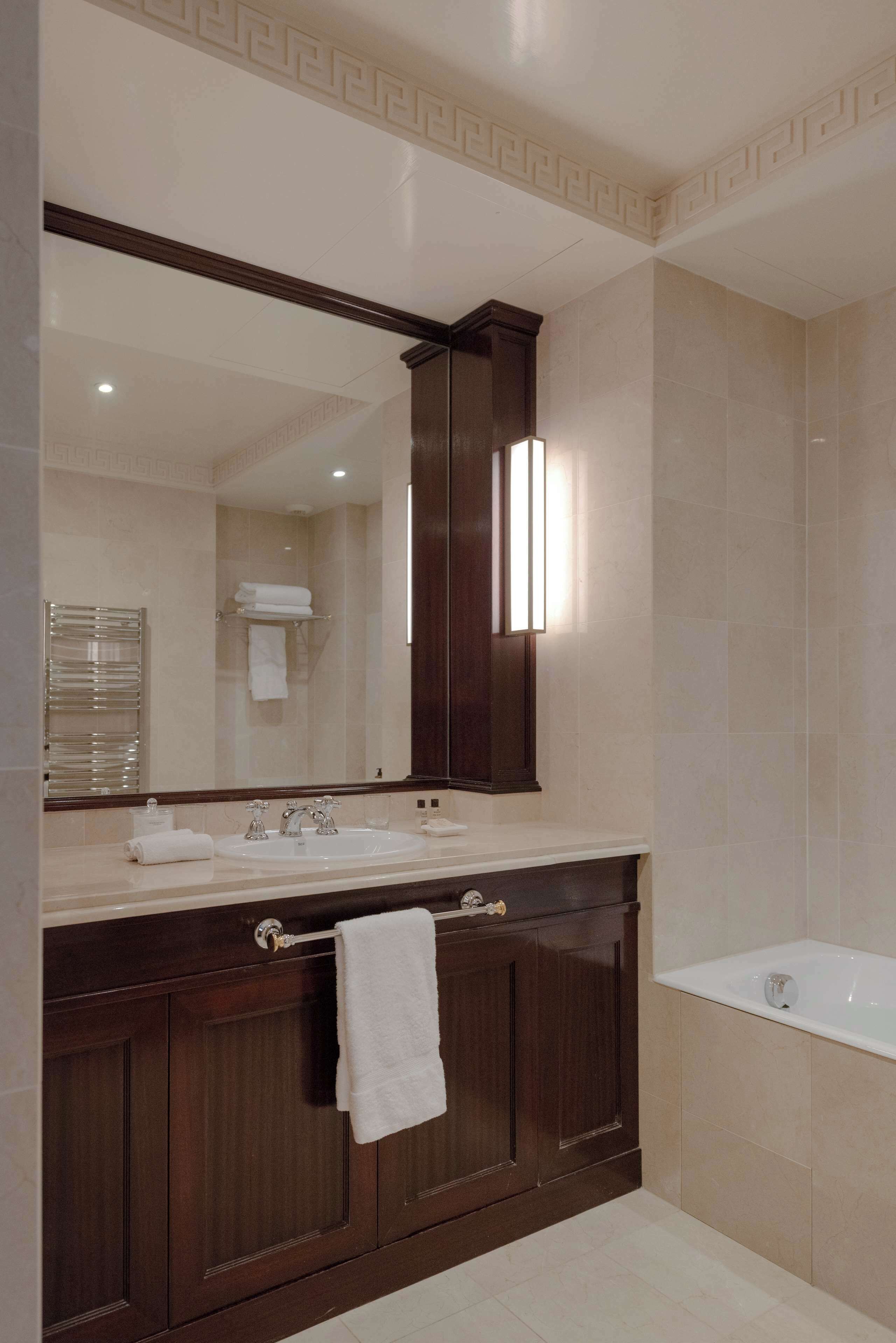 Un baño con un espejo grande, tocador de madera oscura, lavamanos blanco y una bañera.