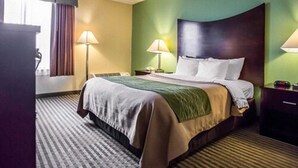 Une chambre d’hôtel avec un lit, deux lampes de chevet, une table de chevet, un bureau et une fenêtre avec des rideaux.
