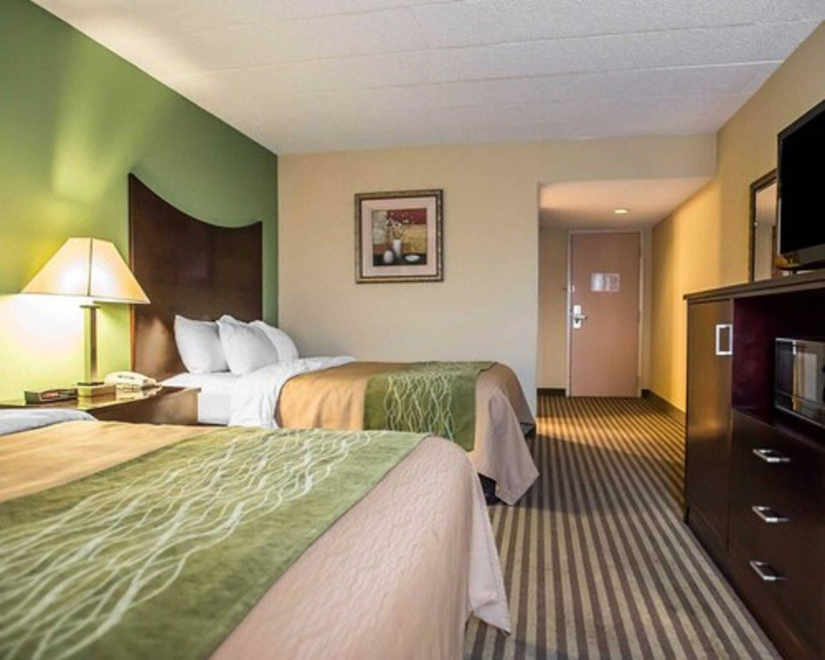 Une chambre d’hôtel avec deux lits, une télévision, un bureau avec une lampe et un tableau au mur.